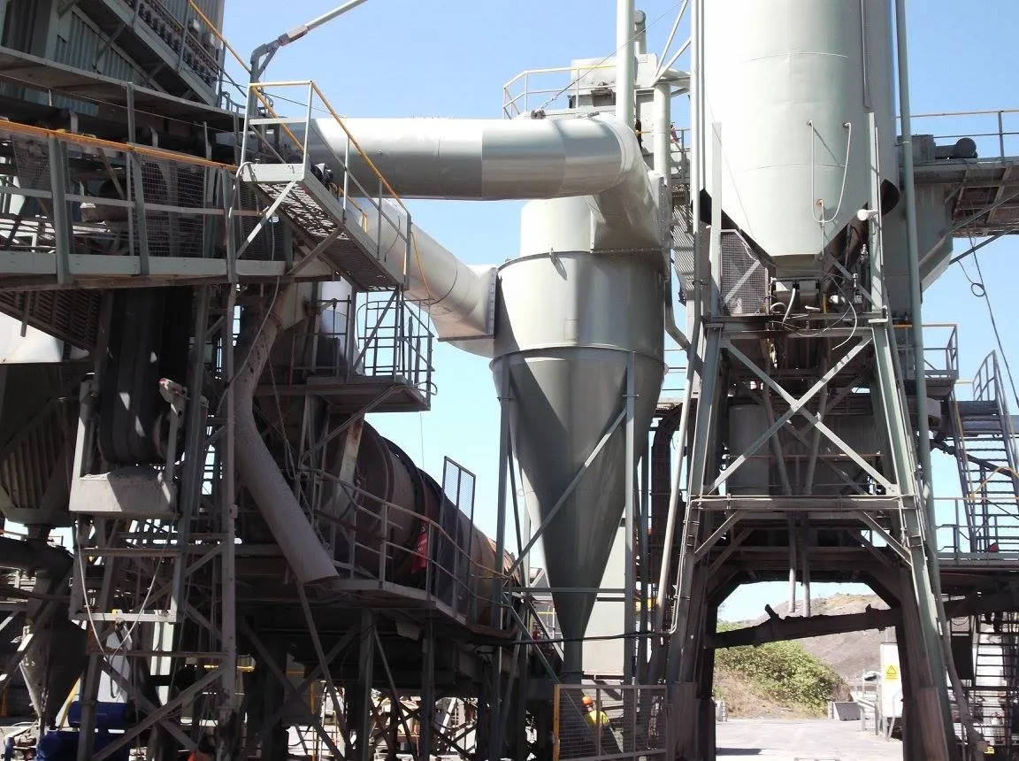 Industrial machinery with large metal tubes, cylindrical containers, and staircases interconnected by a framework of metal beams against a clear blue sky. The equipment appears to be part of a plant or factory, possibly for processing materials.