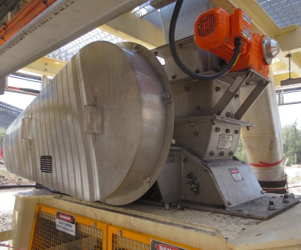 Industrial machinery with a large metal casing and orange motor, set on a platform with safety signs. The background includes metal structures and trees.