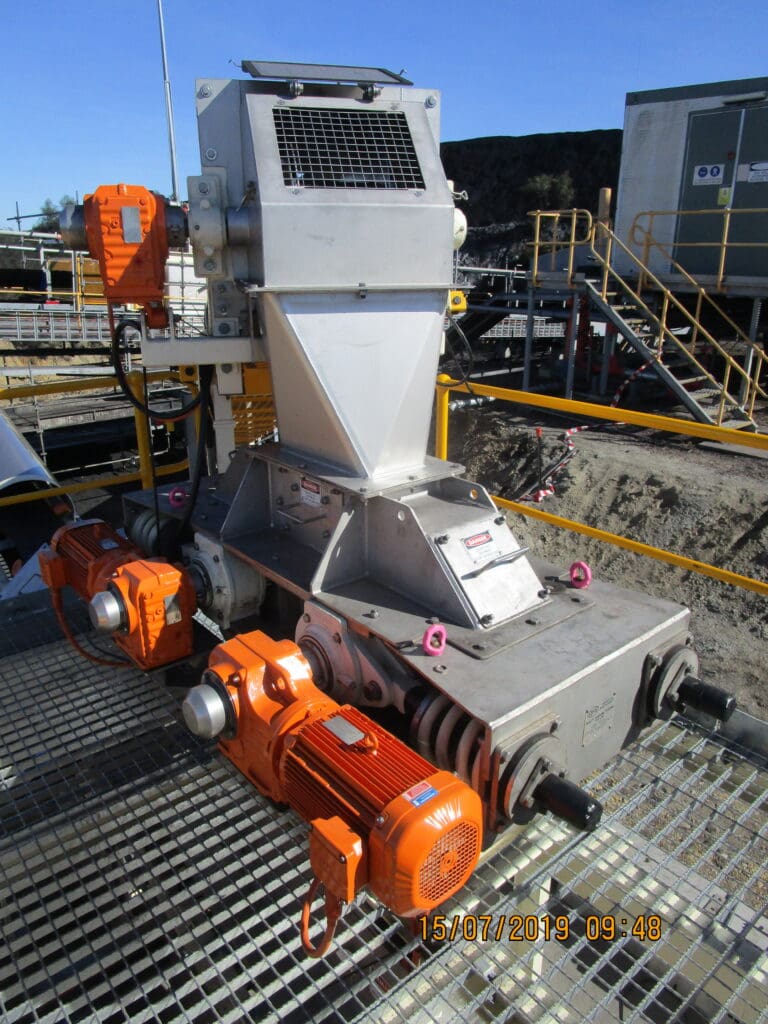 Industrial machinery with a large metal structure featuring orange motors and gears, situated on a grated platform. In the background, there are railings, stairs, and a building. The date on the image reads 15/07/2019 09:48.